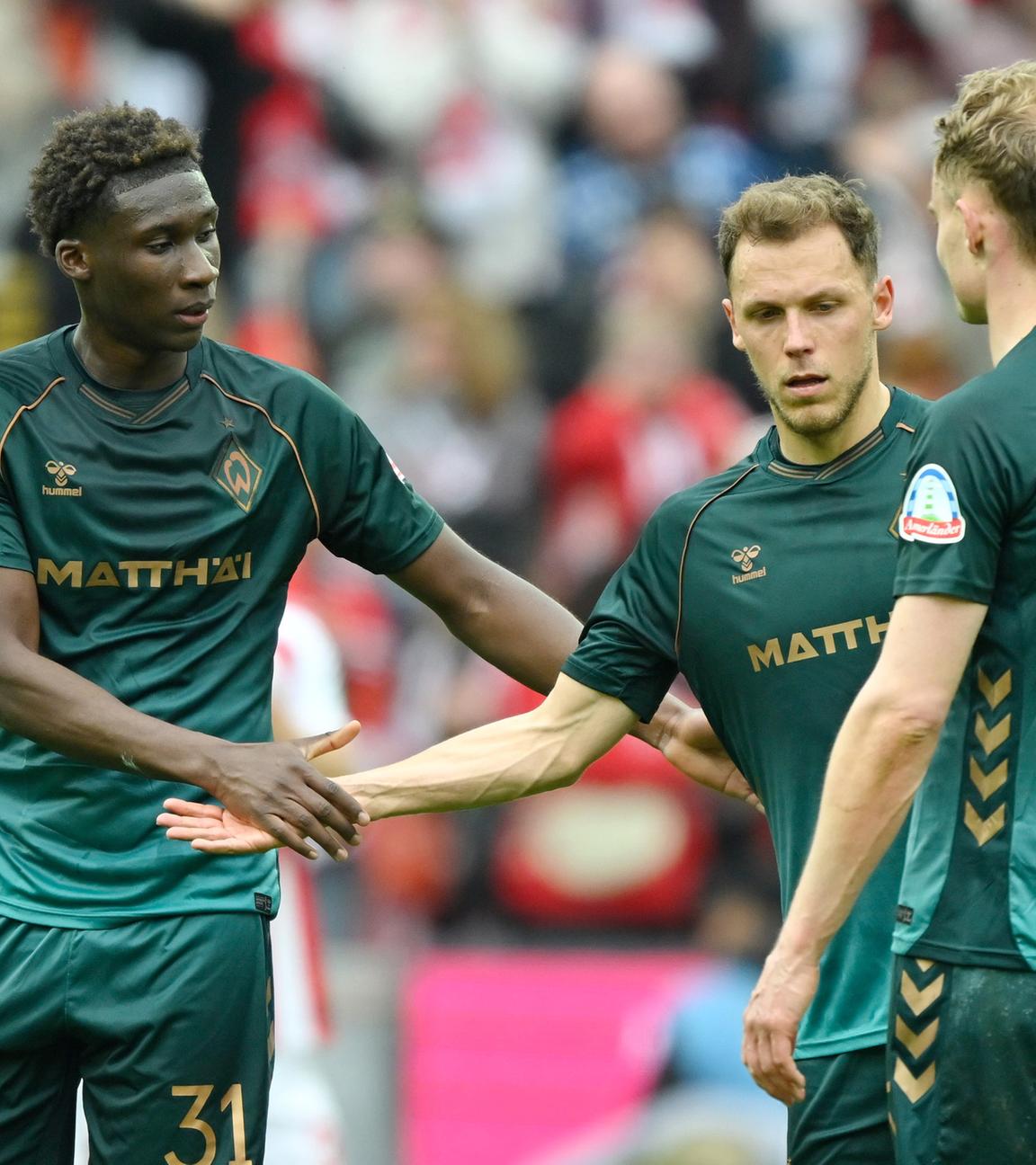 Fußballer Karim Coulibaly, Senne Lynen und Amos Pieper (v.l.) von SV Werder Bremen klatschen sich ab im Spiel gegen den 1. FC Köln am 12.04.2026 in Köln. 