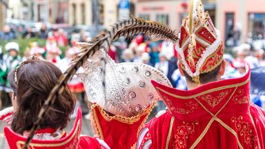 Es sind drei Personen von hinten zu sehen. Auf dem Bild ist Karneval und alle drei sind verkleidet.