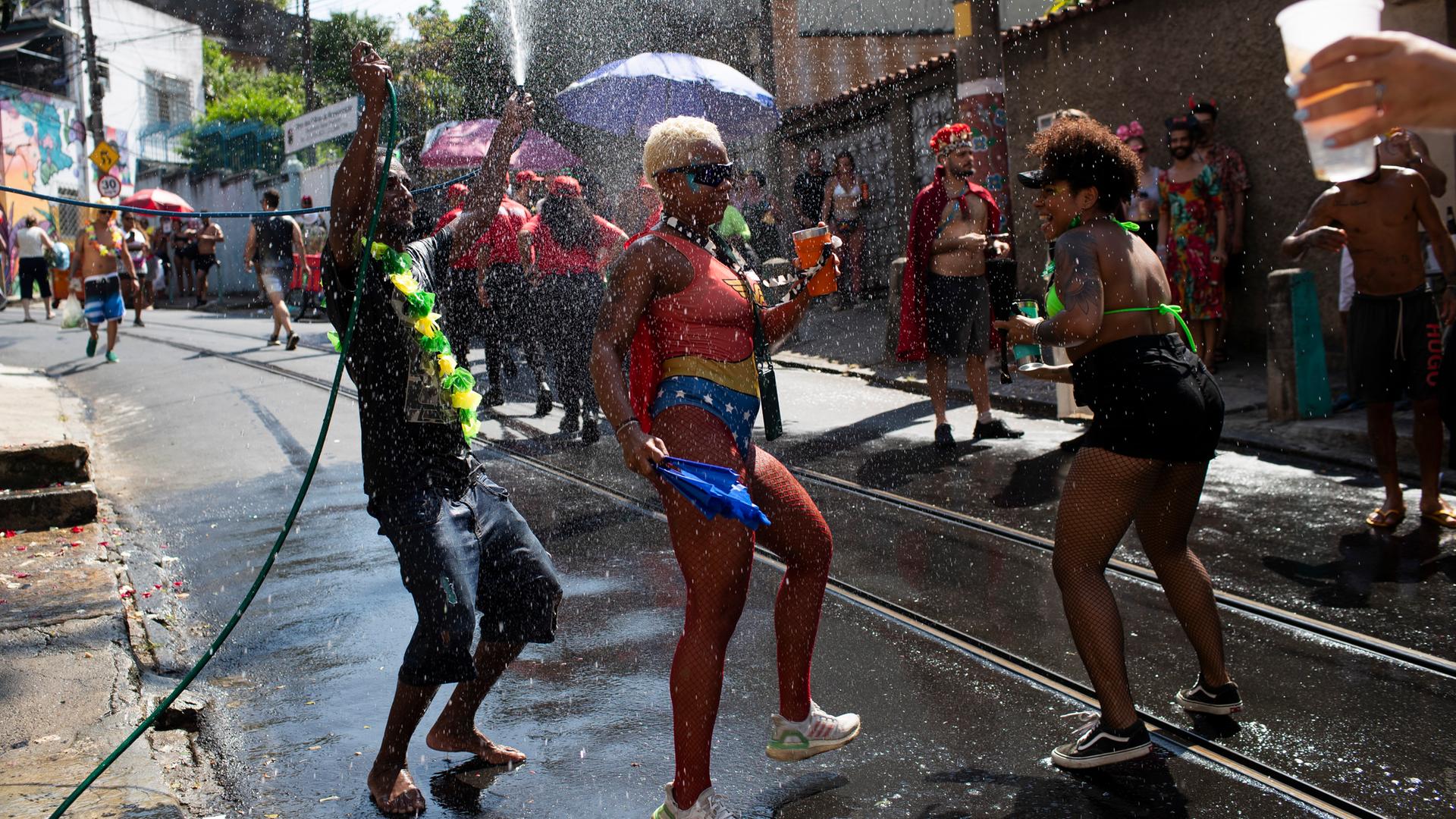Brazil CEin Feiernder bespritzt seine Mitfeiernden mit Wasser, um sie während des Straßenfestesabzukühlen, während einer Hitzewelle in Rio de Janeiro, Samstag, 22.02.2025.