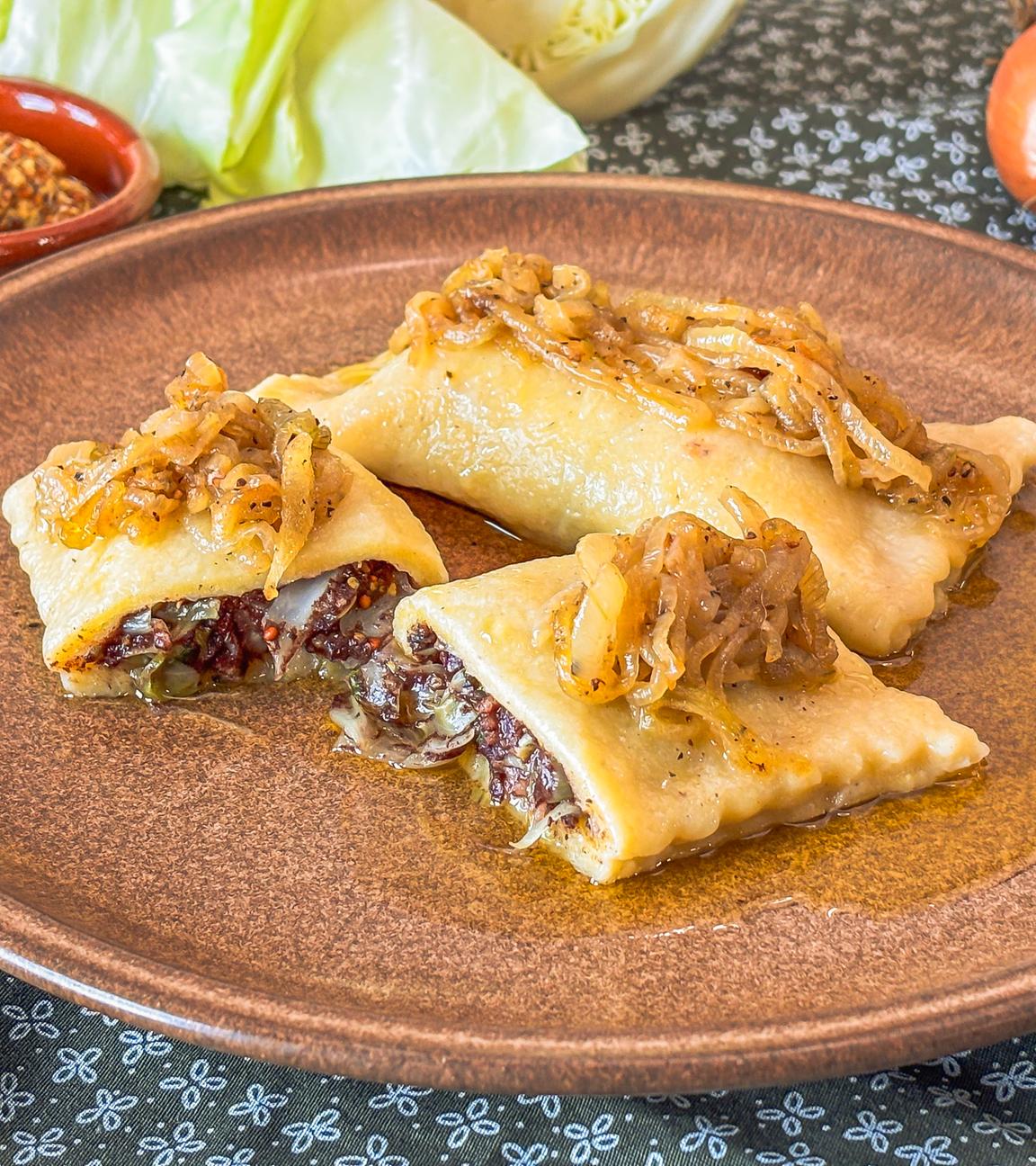 Brauner Teller mit Kartoffelmaultaschen, gefüllt mit Blutwurst und getoppt mit Schmorzwiebeln.