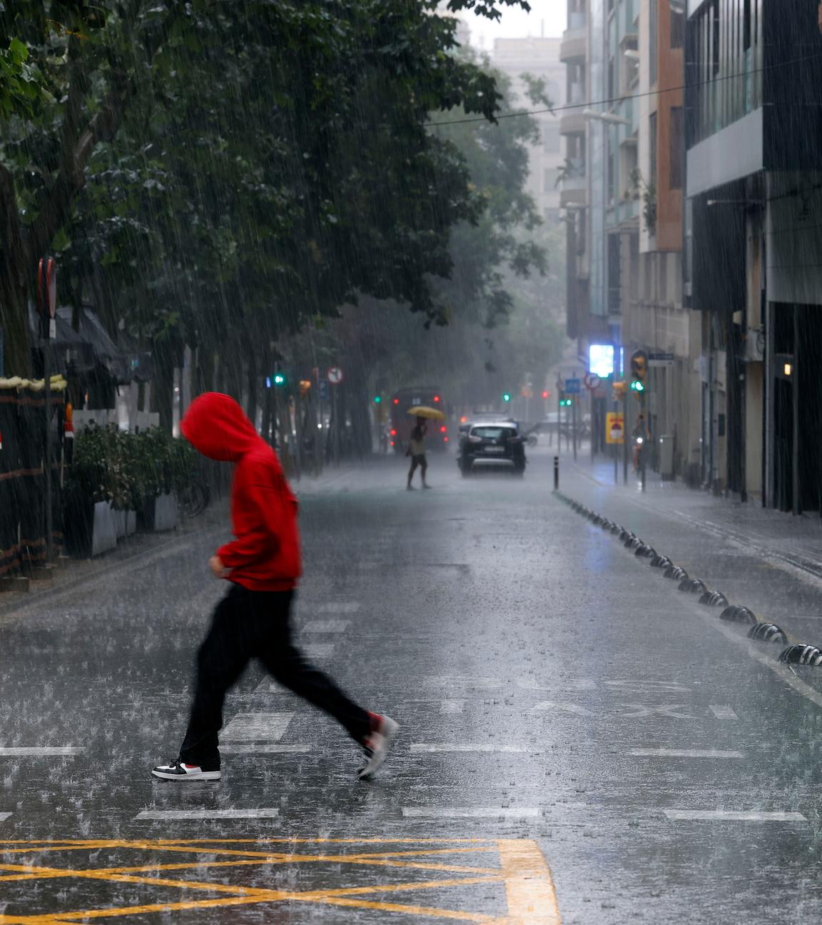 Menschen überqueren im Regen eine Straße in Barcelona