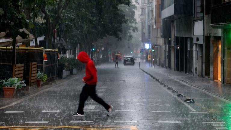 Menschen überqueren im Regen eine Straße in Barcelona