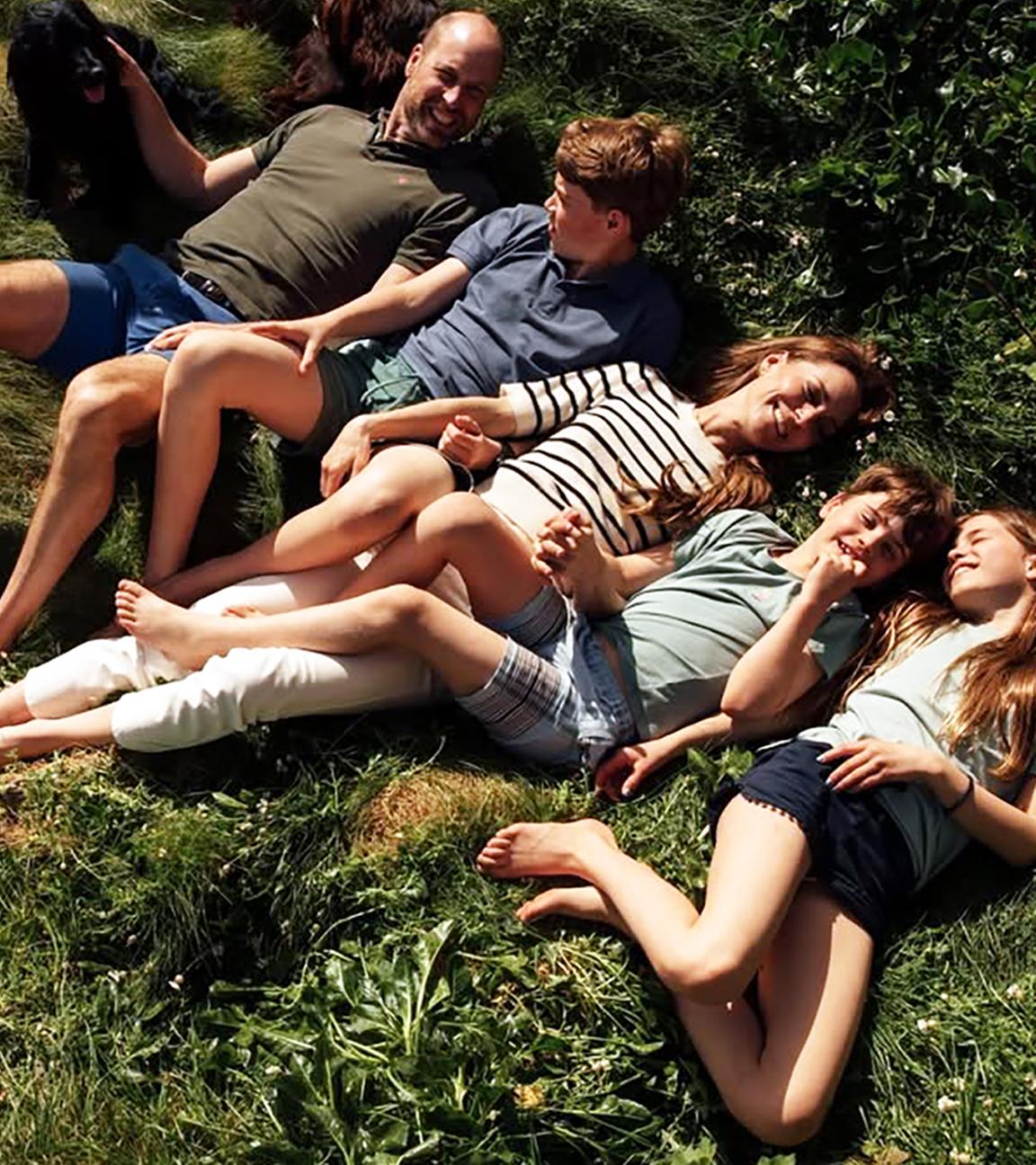 Ein Bild von Kate und William, wie sie mit ihren drei Kindern auf einer Grasfläche liegen und lächeln.