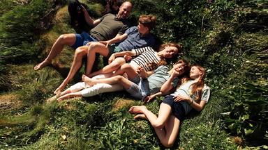 Ein Bild von Kate und William, wie sie mit ihren drei Kindern auf einer Grasfläche liegen und lächeln.