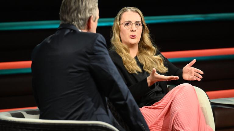 Grünen-Politikerin Katharina Dröge sitzt mit einem schwarzen Oberteil und einem korallfarbenden Rock im TV-Studio bei Markus Lanz.