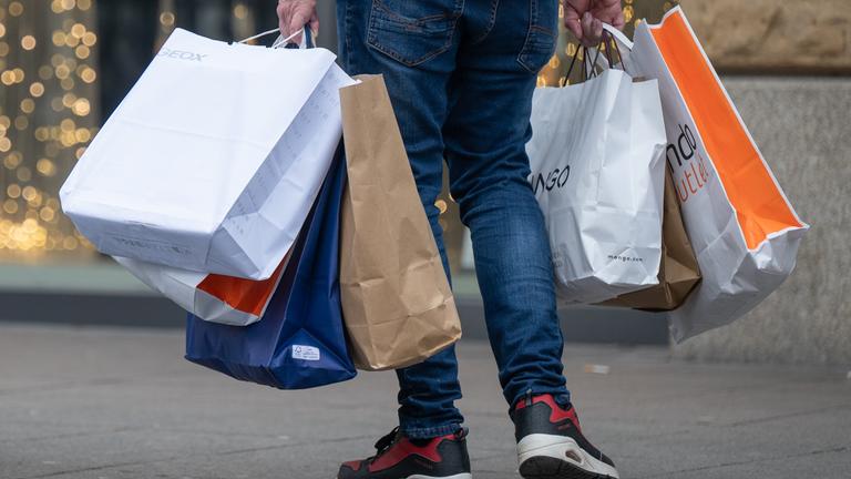 Ein Mann trägt sieben Einkaufstüten in beiden Händen.