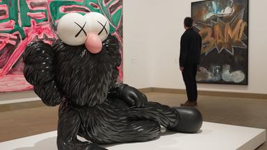 Skulptur in Übergröße liegt in einem Museum. Die Skulptur ist eine große, Comicartige Figur in schwarz. 