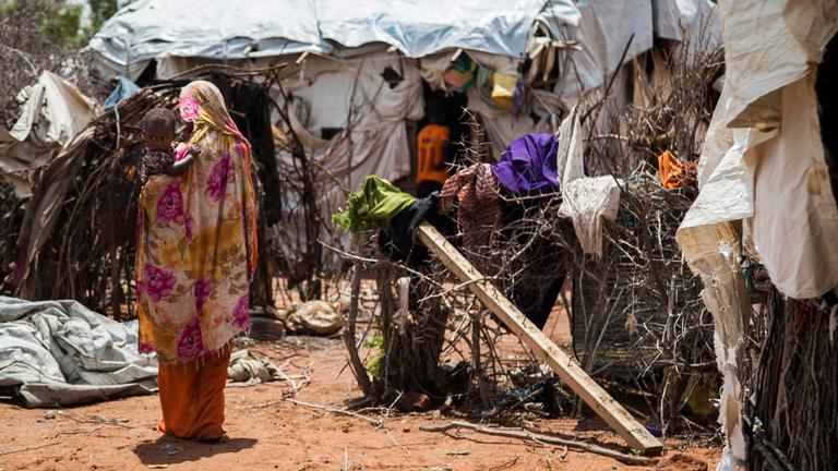 Eine Frau hat ein Kind auf dem Arm und steht mit dem Rücken zur Kamera in einem Flüchtlingslager in Kenia.