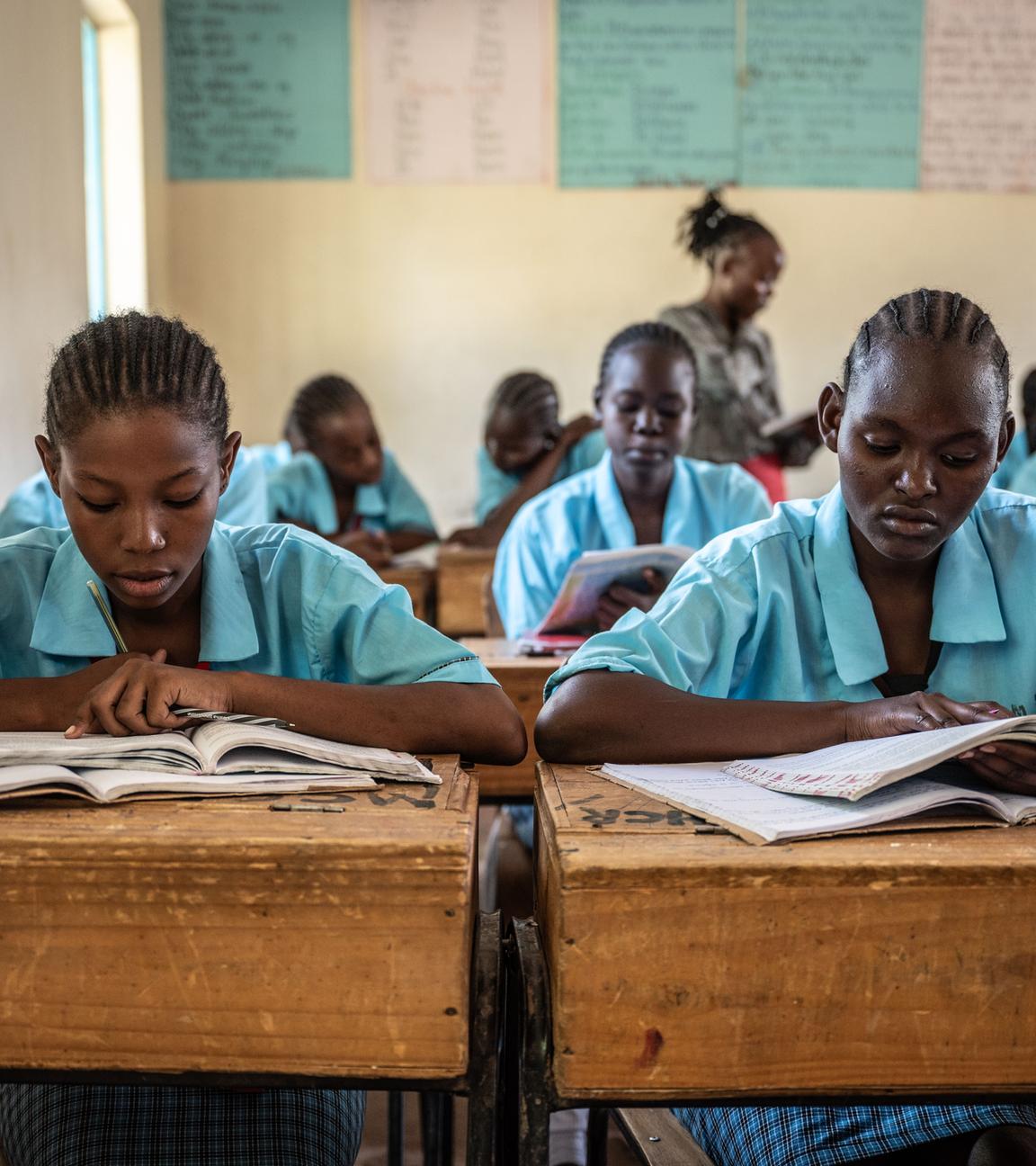Kenianische Schülerinnen in hellblauer Schuluniform im Unterricht an ihren Bänken über ihren Lernmaterialien.