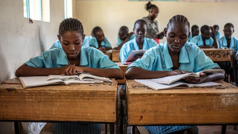 Kenianische Schülerinnen in hellblauer Schuluniform im Unterricht an ihren Bänken über ihren Lernmaterialien.