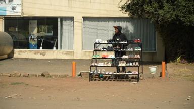 Ein junger Mann steht an einer Straße in Kiserian (Kenia) und verkauft Schuhe.