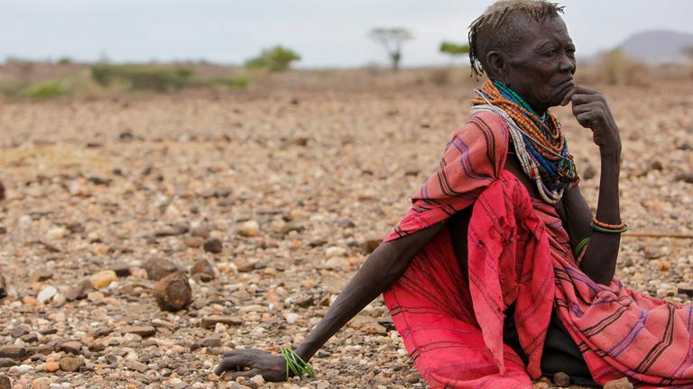 Frau sitzt in kenianischer Wüstenlandschaft