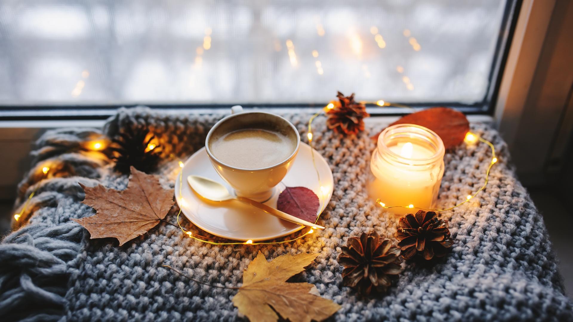 Eine Kerze, eine Tasse Kaffee und Herbstdekoration auf einer Fensterbank.