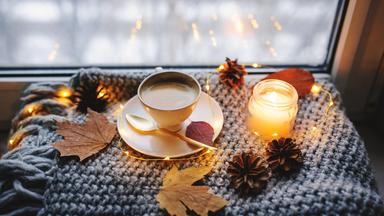 Eine Kerze, eine Tasse Kaffee und Herbstdekoration auf einer Fensterbank.