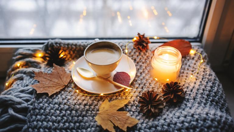 Eine Kerze, eine Tasse Kaffee und Herbstdekoration auf einer Fensterbank.
