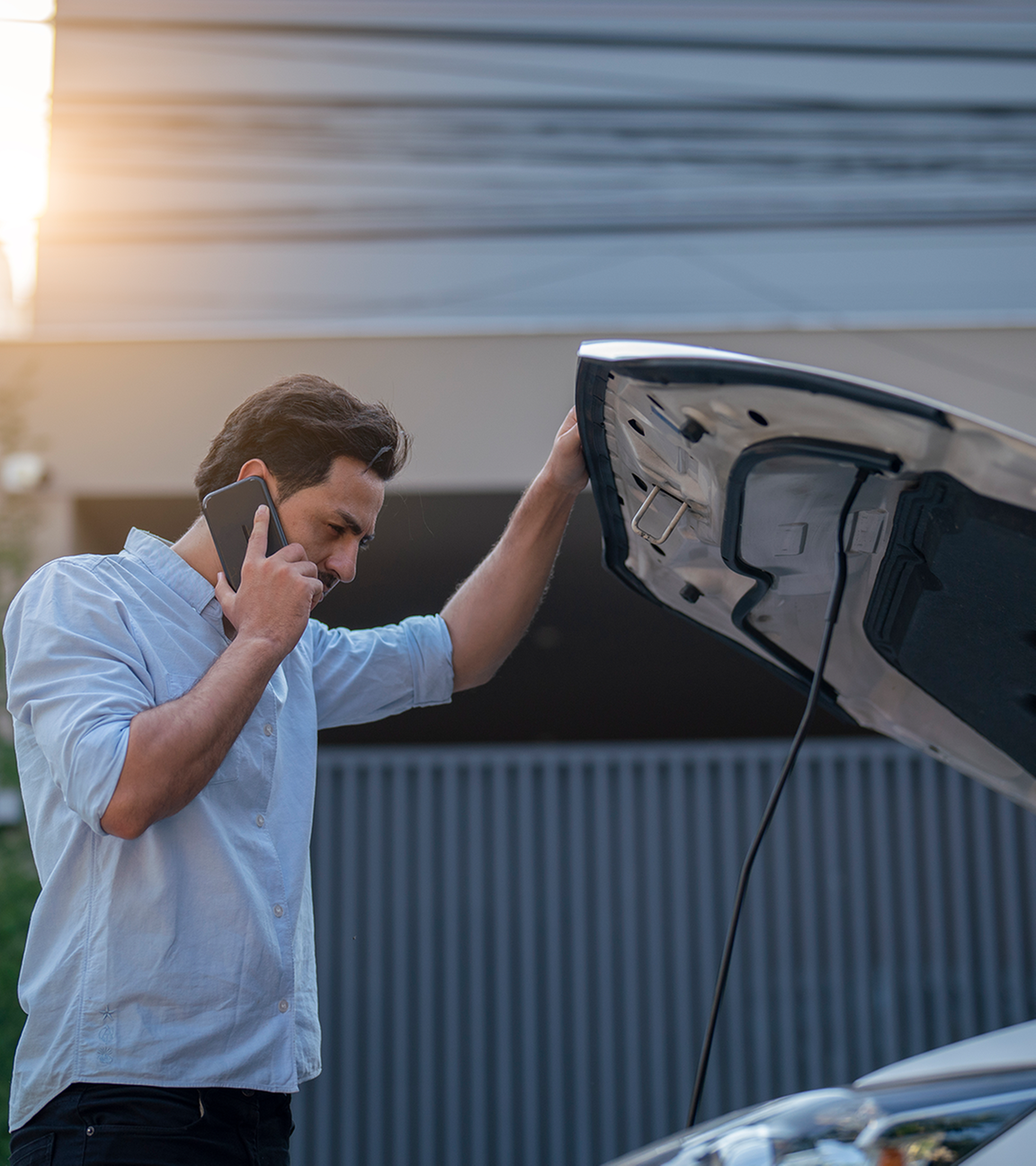 Mann hat die Motorhaube seines Autos geöffnet und telefoniert