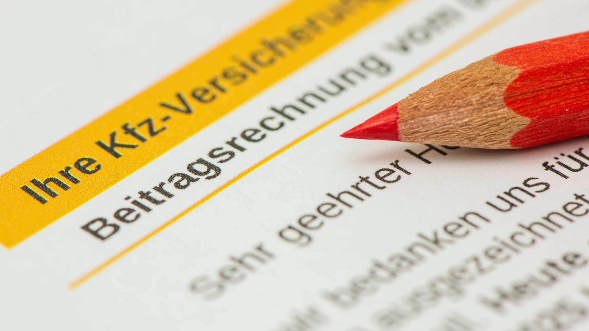 Ausschnitt eines Kfz-Versicherungsvertrags mit der Aufschrift "Ihre Kfz-Versicherung" und "Beitragsrechnung". Auf dem Papier liegt ein roter Buntstift.