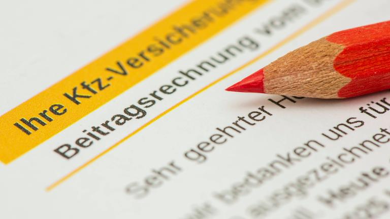 Ausschnitt eines Kfz-Versicherungsvertrags mit der Aufschrift "Ihre Kfz-Versicherung" und "Beitragsrechnung". Auf dem Papier liegt ein roter Buntstift.