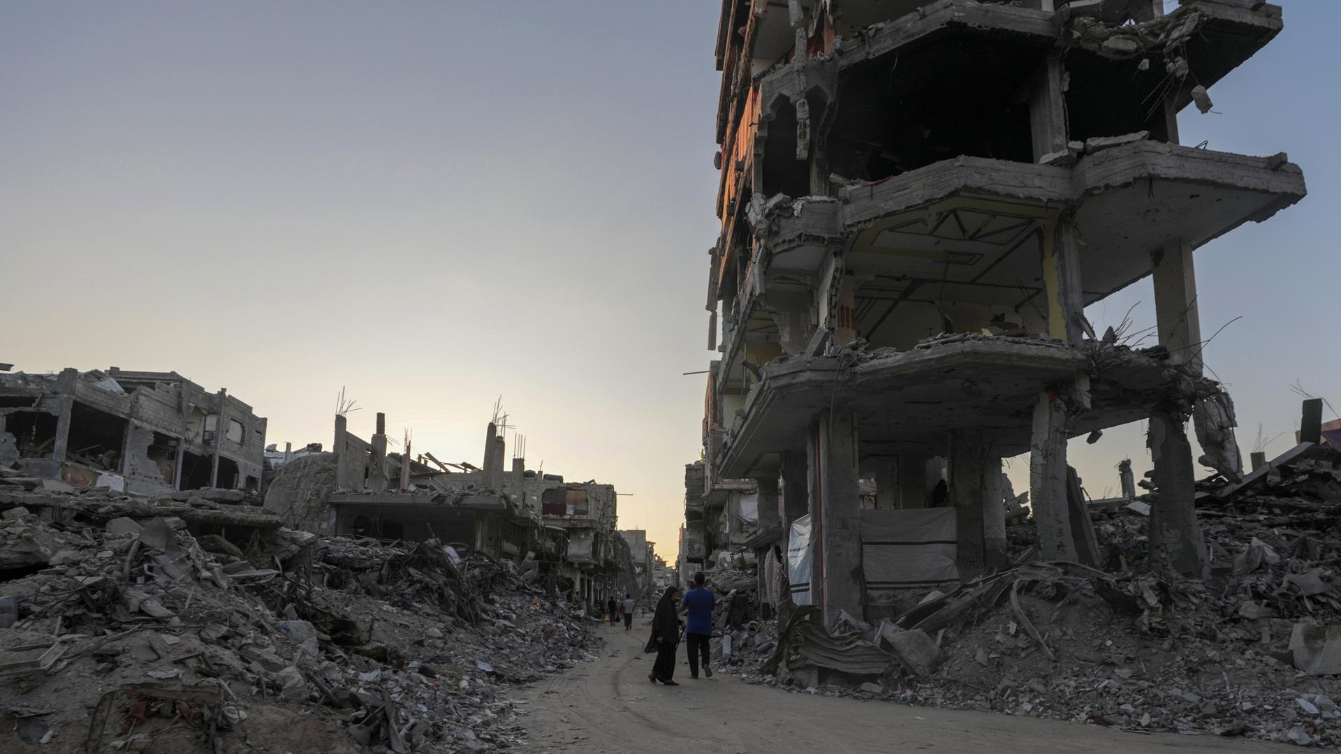 Palästinenser gehen an einem zerstörten Gebäude vorbei durch die Straßen von Khan Younis, südlicher Gazastreifen, 04.08.2024.