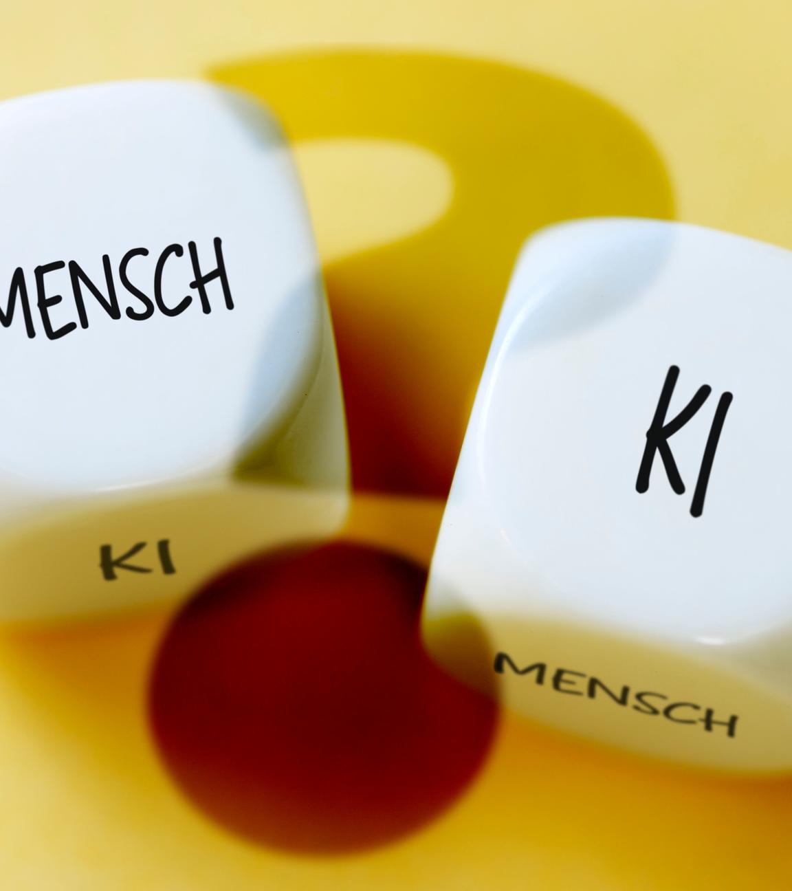 Es sind zwei Würfel zu sehen mit der jeweiligen Aufschrift "KI" und "Mensch"