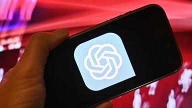 Hand zeigt ein Smartphone mit dem ChatGPT Logo vor rotem Hintergrund