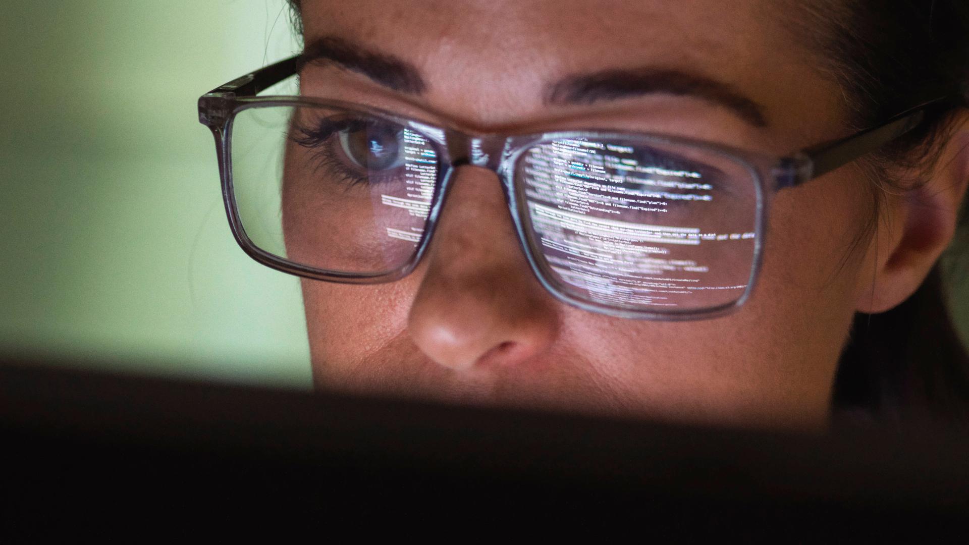 Frau blickt auf den Laptop-Bildschirm, der sich im Glas ihrer Brille spiegelt.