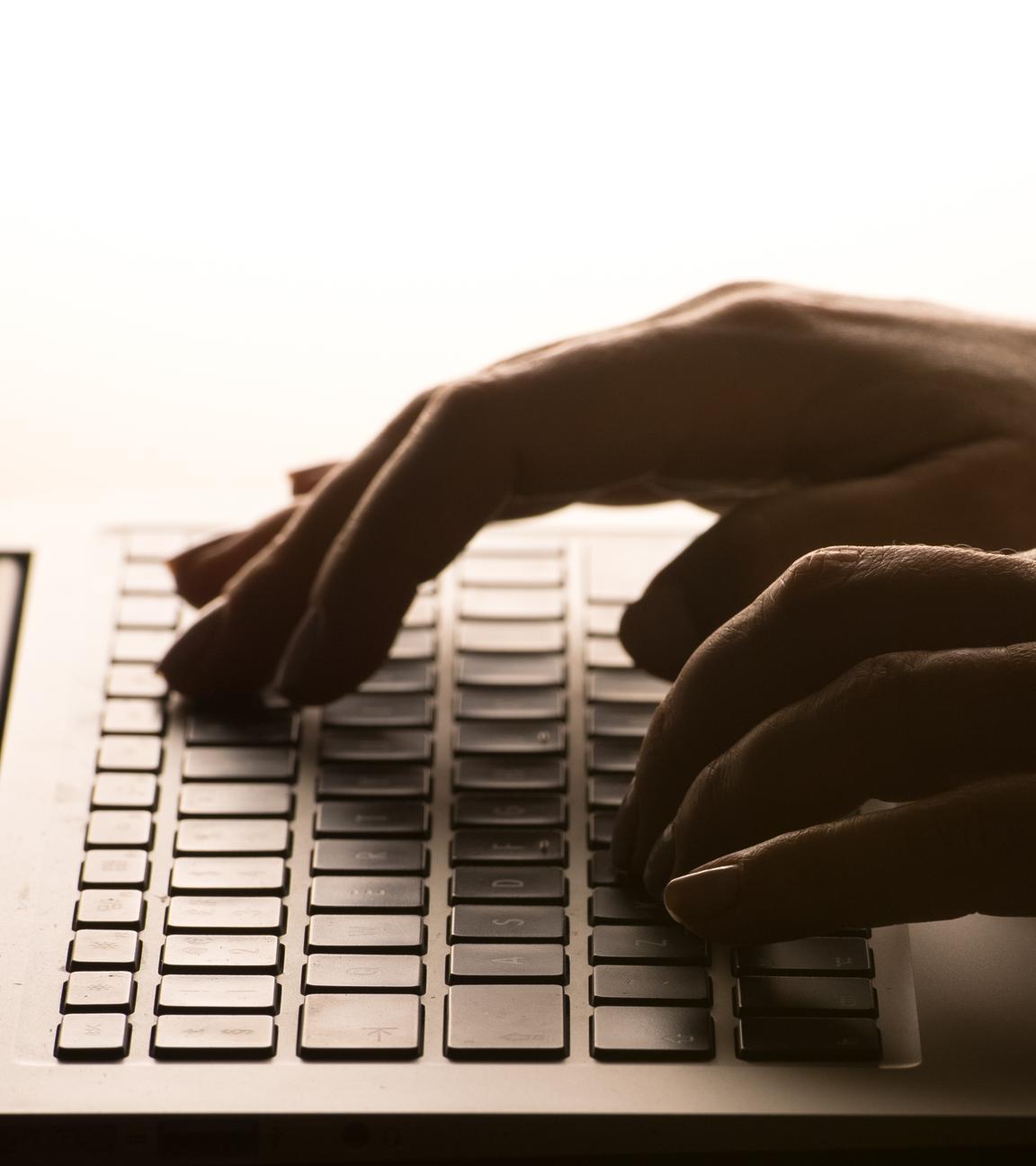 Die Hände einer Person, die auf die Tastatur eines Laptops tippt.