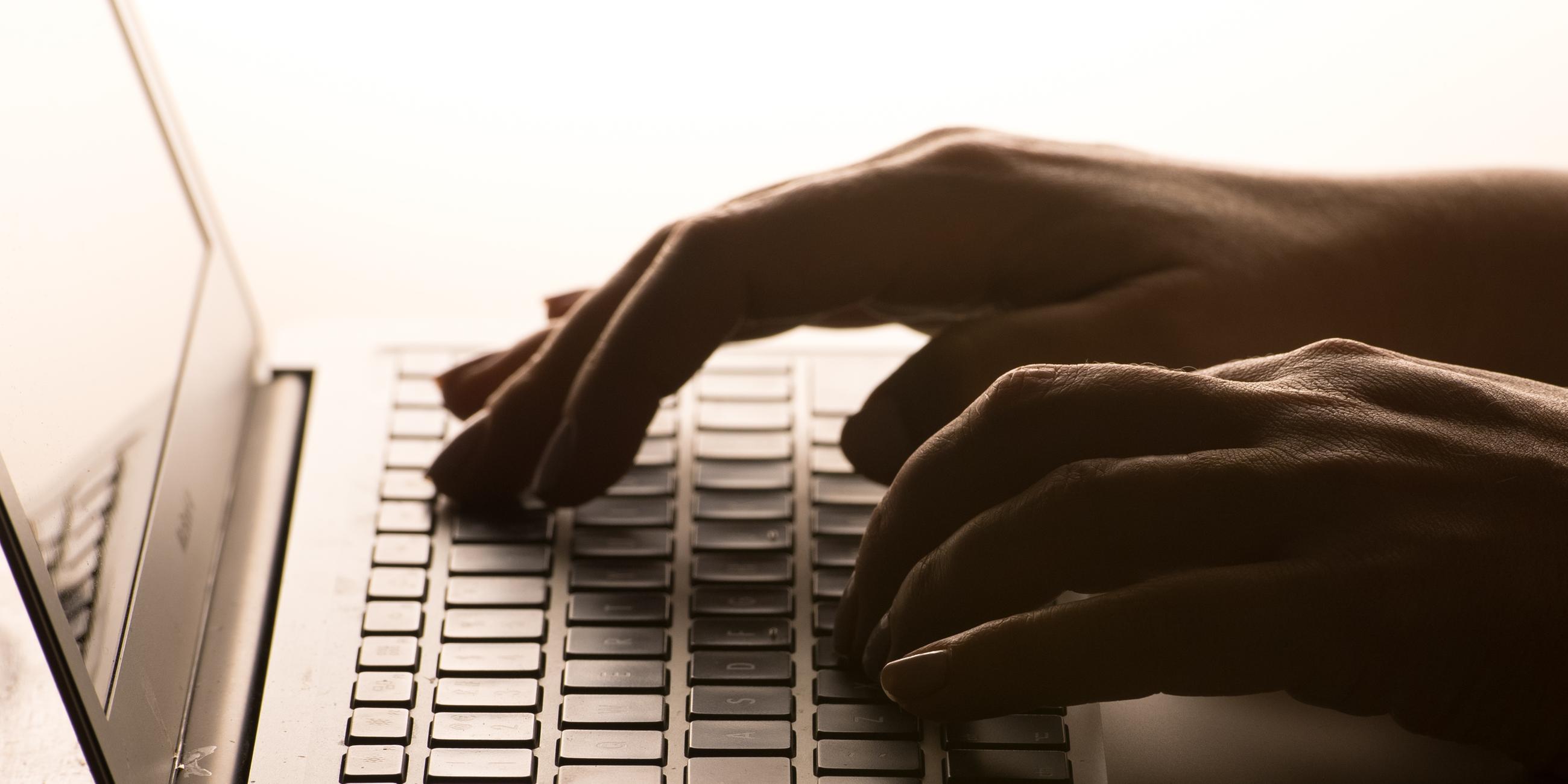 Die Hände einer Person, die auf die Tastatur eines Laptops tippt.