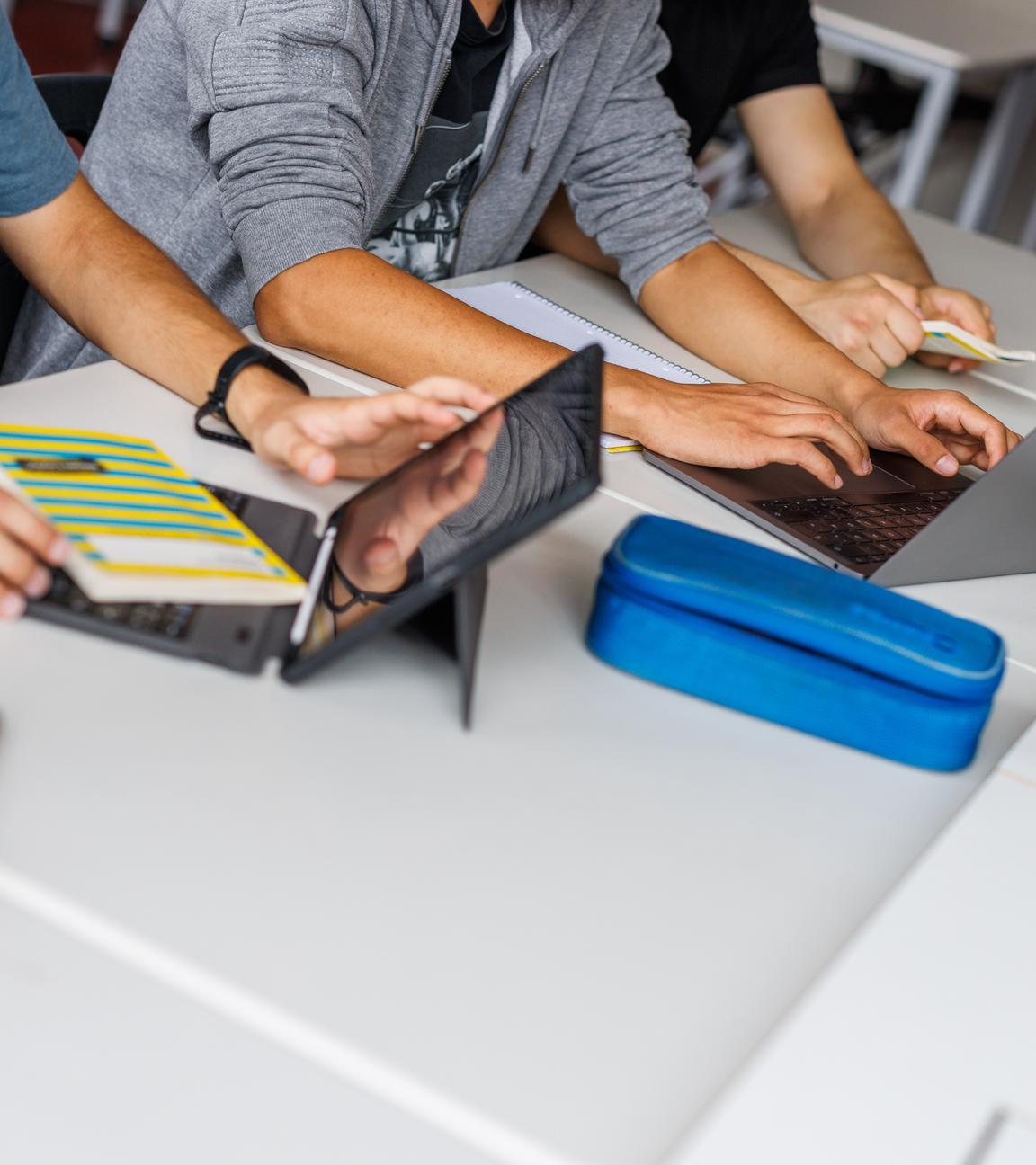 Schüler eines Gymnasiums sitzen vor einem Laptop und benutzen ein KI-Tool.