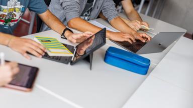 Schüler eines Gymnasiums sitzen vor einem Laptop und benutzen ein KI-Tool.