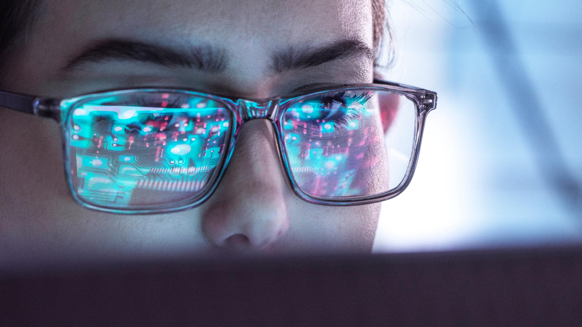 Eine Frau mit Brille blickt auf einen Computerbildschirm.