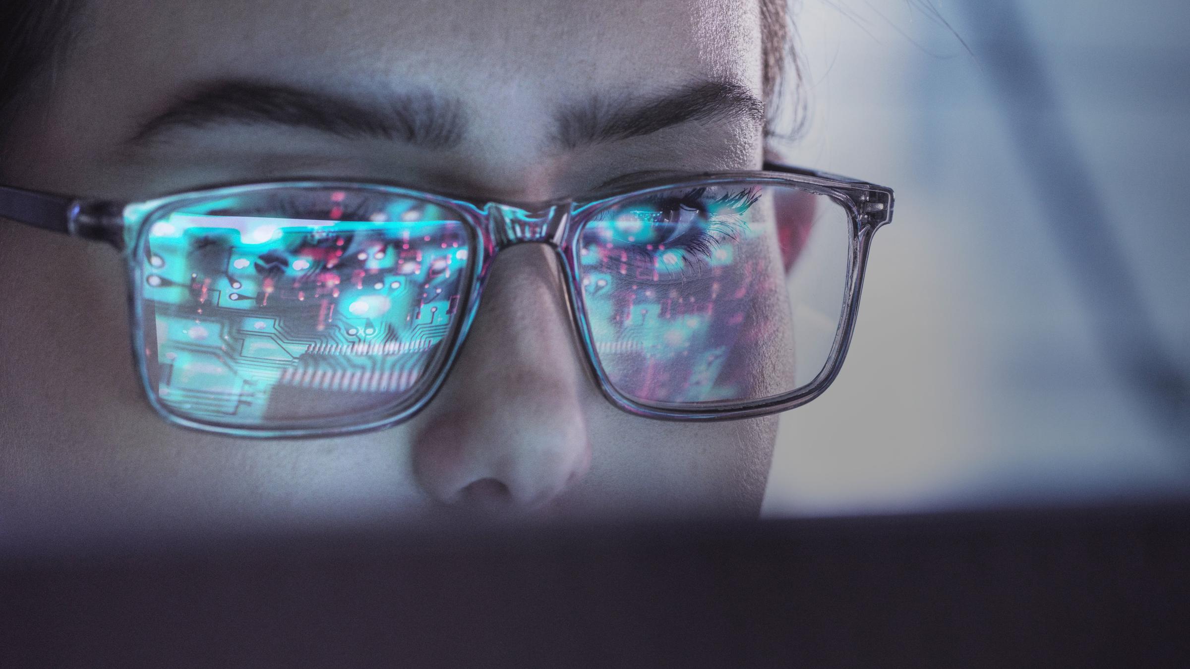 Eine Frau mit Brille blickt auf einen Computerbildschirm.