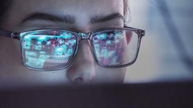 Eine Frau mit Brille blickt auf einen Computerbildschirm.