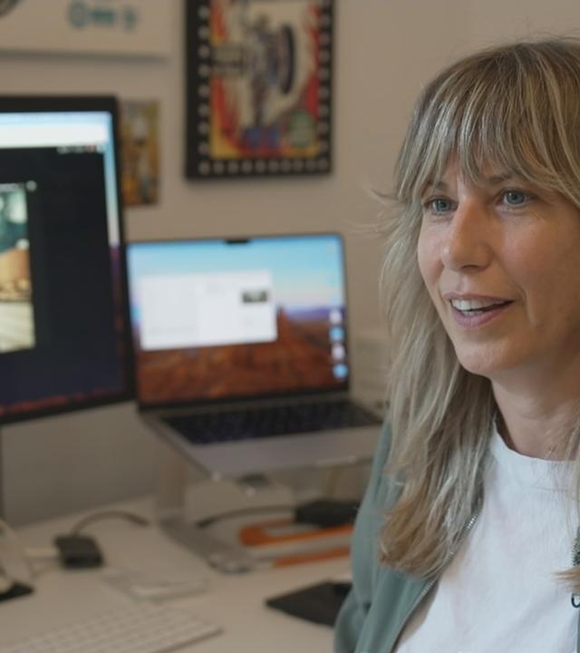 Alexandra Lier sitzt an einem Schreibtisch mit Computer, auf dem Bildschirm ist eines ihrer KI-Kunstwerke zu sehen