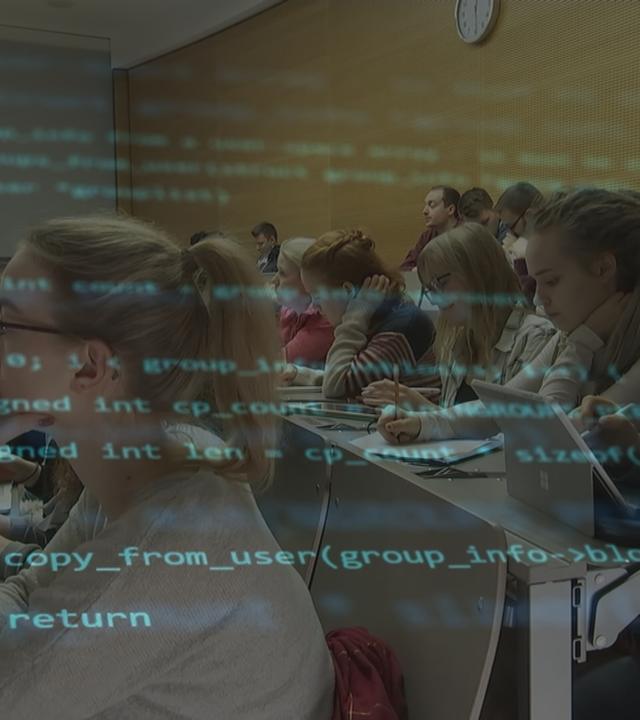 Eine Computerschrift liegt über einem Bild von Studierenden im Vorlesungsraum