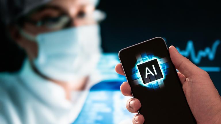 Im Vordergrund ist ein Telefon mit einem AI-Logo, im Hintergrund eine Person in medizinischer Kleidung und Mundschutz.