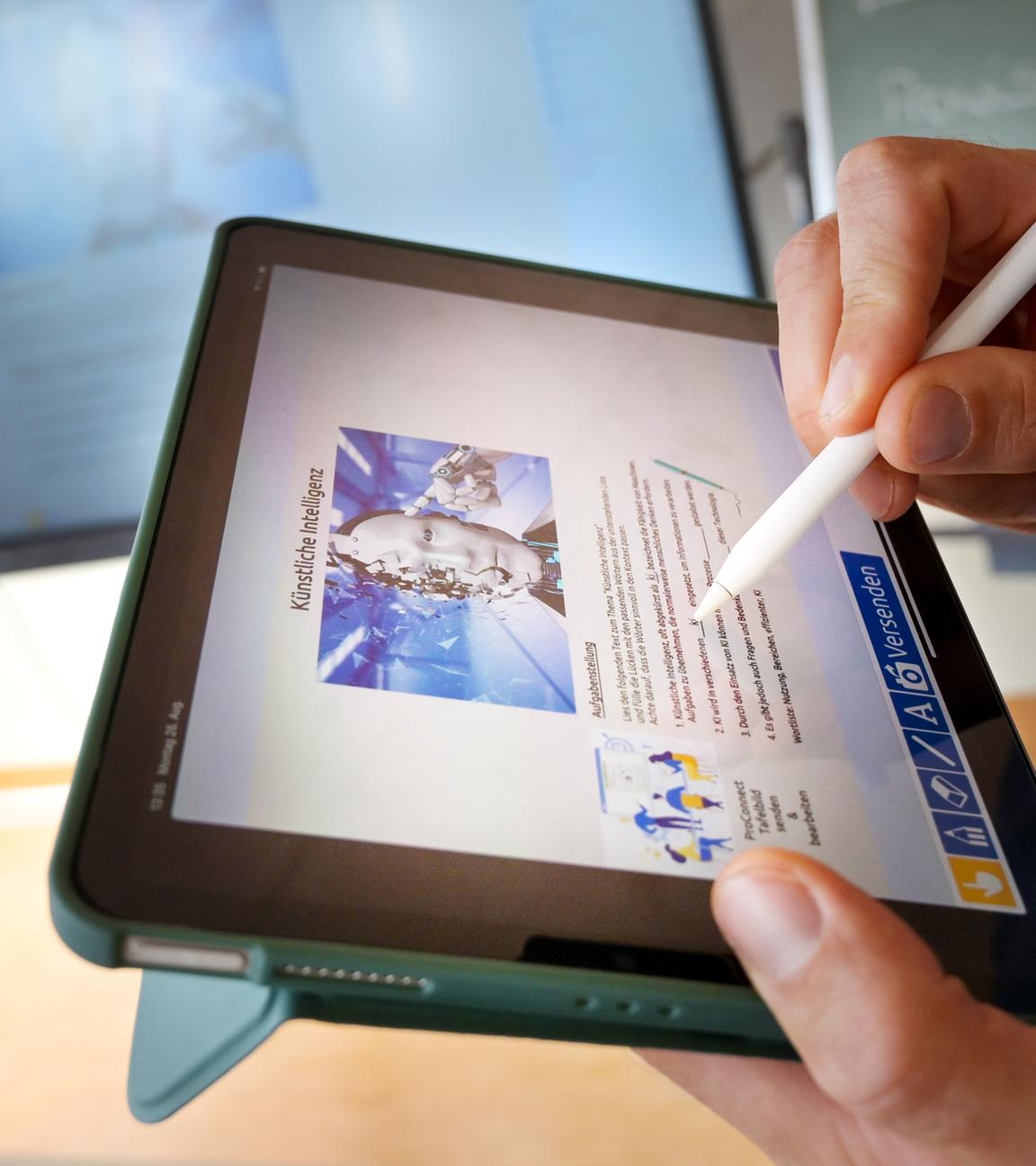 Lehrperson hält Tablet in der Hand, im Hintergrund sind zwei Schultafeln zu sehen.