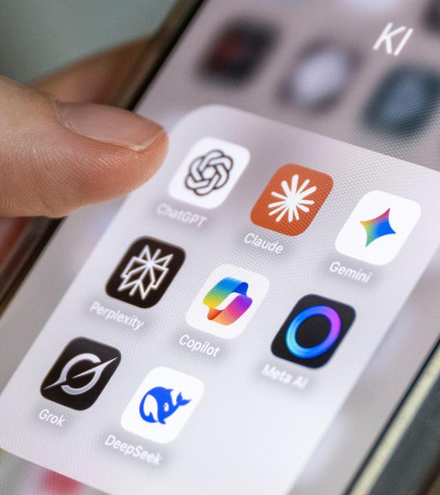 Auf einem Smartphone-Bildschirm sind mehrere KI-Anwendungen zu sehen, darunter ChatGPT, Claude, Gemini, Perplexity, Microsoft Copilot, Meta AI, Grok und DeepSeek. Die Apps sind in einem Ordner mit der Bezeichnung "KI" gruppiert.