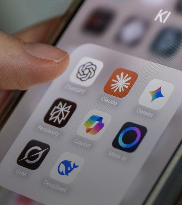 Auf einem Smartphone-Bildschirm sind mehrere KI-Anwendungen zu sehen, darunter ChatGPT, Claude, Gemini, Perplexity, Microsoft Copilot, Meta AI, Grok und DeepSeek. Die Apps sind in einem Ordner mit der Bezeichnung "KI" gruppiert.