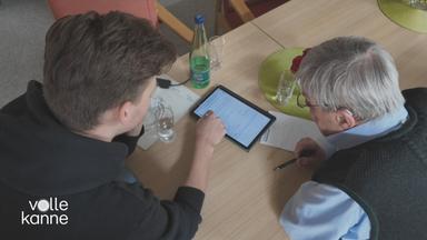 Junger Mann zeigt altem Mann etwas auf einem Tablett