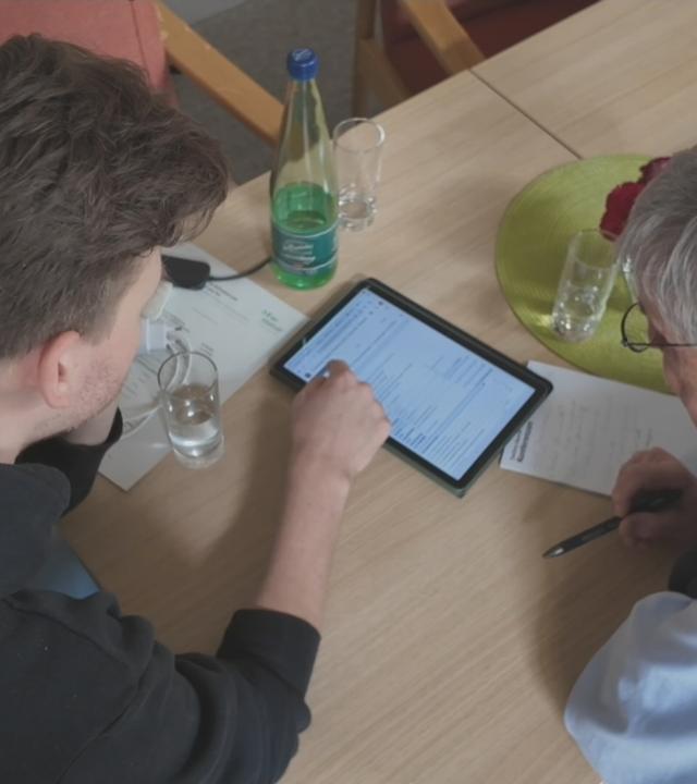 Junger Mann zeigt altem Mann etwas auf einem Tablett
