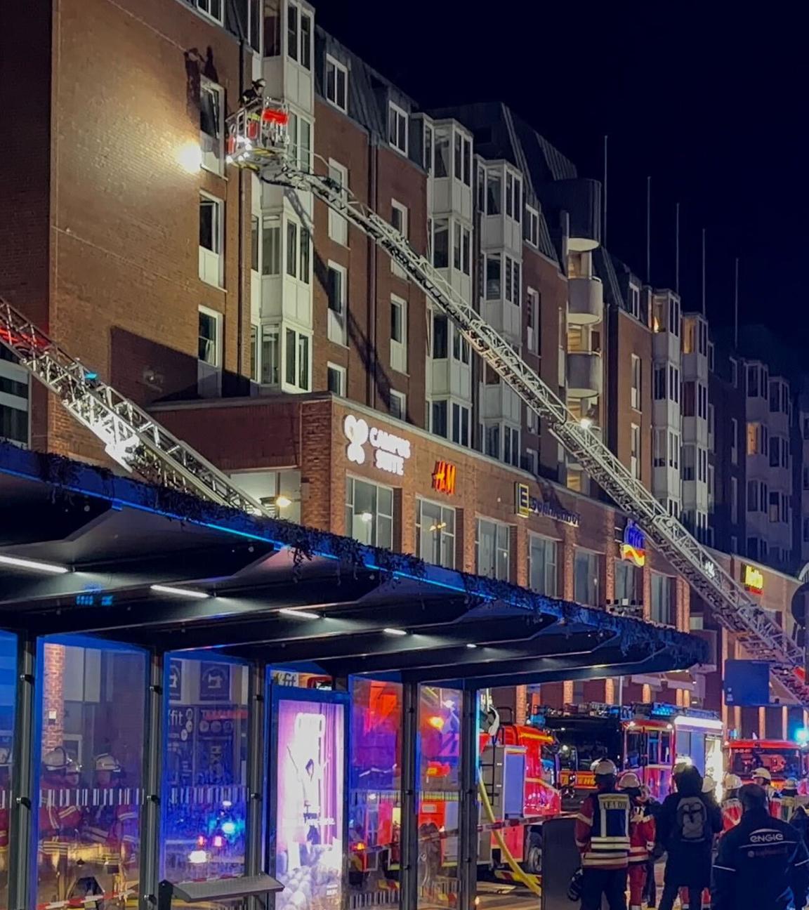 Einsatzkräfte der Feuerwehr arbeiten auf Drehleitern an einem Wohnhaus neben dem Einkaufszentrum Sophienhof in der Kieler Innenstadt