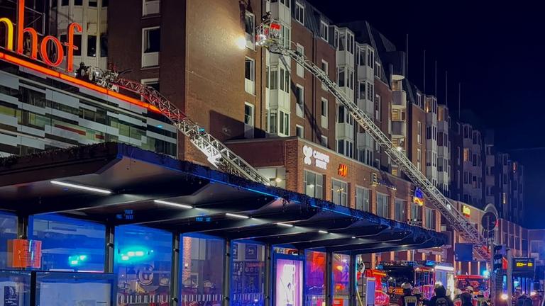 Einsatzkräfte der Feuerwehr arbeiten auf Drehleitern an einem Wohnhaus neben dem Einkaufszentrum Sophienhof in der Kieler Innenstadt