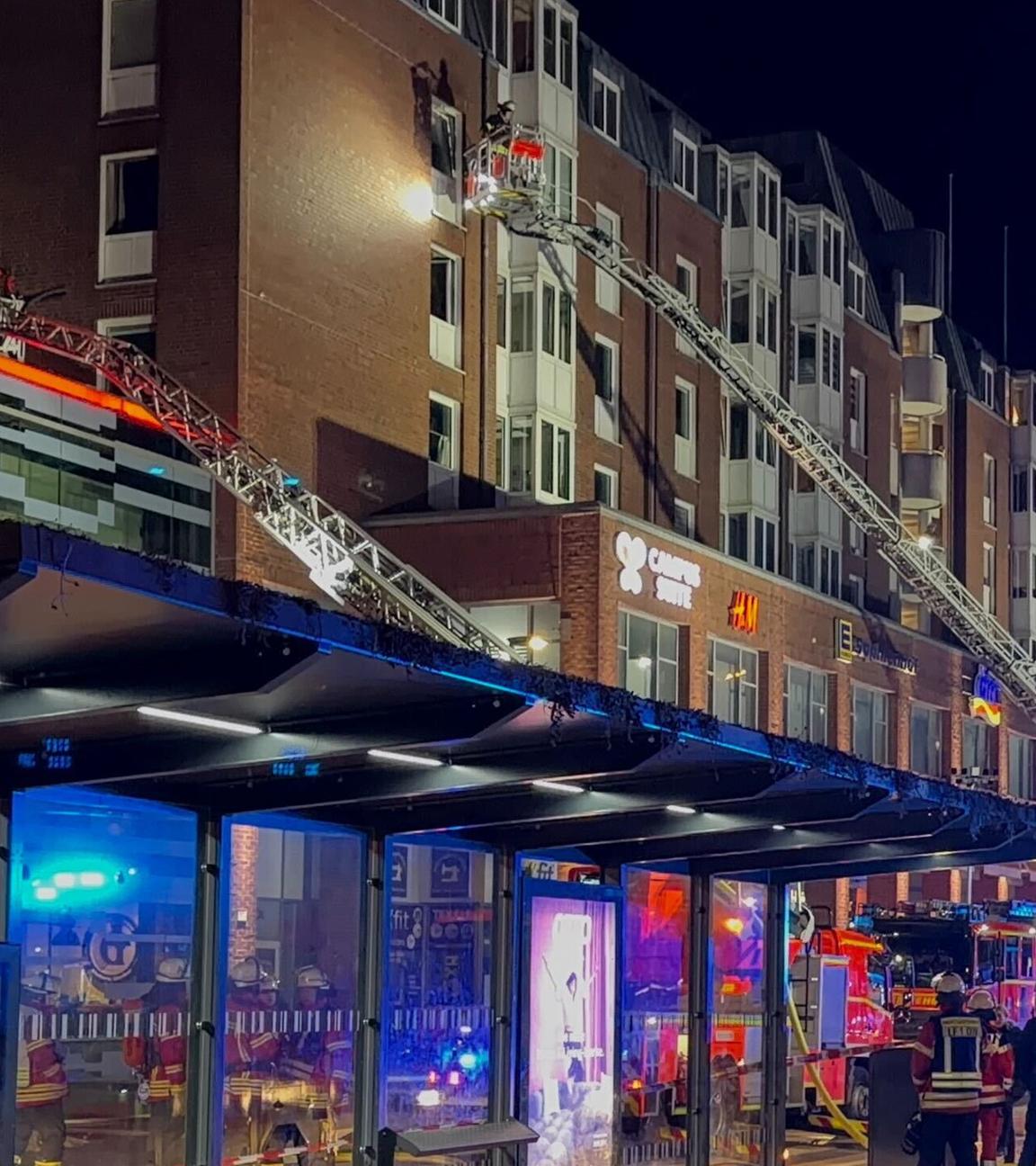 Einsatzkräfte der Feuerwehr arbeiten auf Drehleitern an einem Wohnhaus neben dem Einkaufszentrum Sophienhof in der Kieler Innenstadt in dem ein Brand ausgebrochen war. 