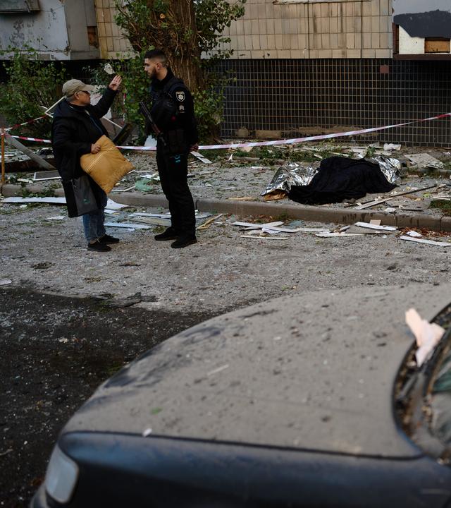 Ein Polizist spricht mit einem Anwohner neben den Leichen zweier Menschen, die bei einem nächtlichen russischen Angriff ums Leben gekommen sind. 