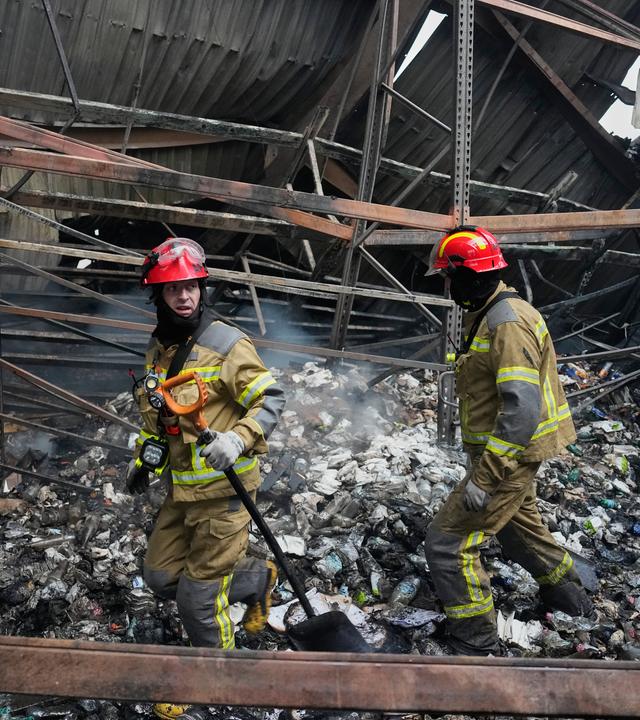 Ukrainische Feuerwehrmänner stehen in einem zerstörten Haus