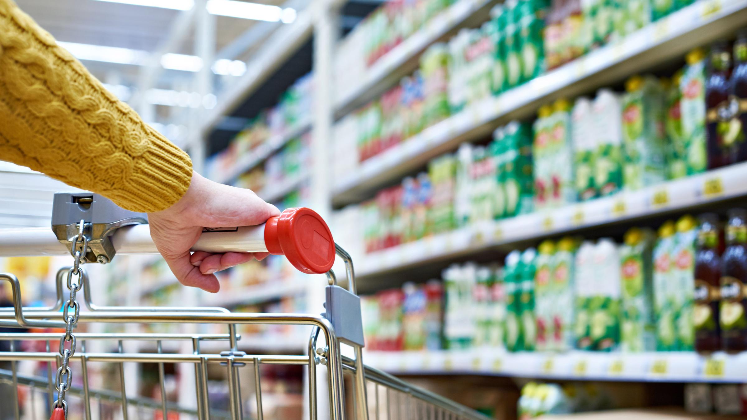 Das Bild zeigt wie eine Frau einen Einkaufswagen durch einen Supermarkt schiebt.