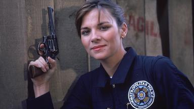 Kim Cattrall als Polizeischülerin in der Serie "Police Academy - Dümmer als die Polizei erlaubt" mit einer Waffe in der Hand.