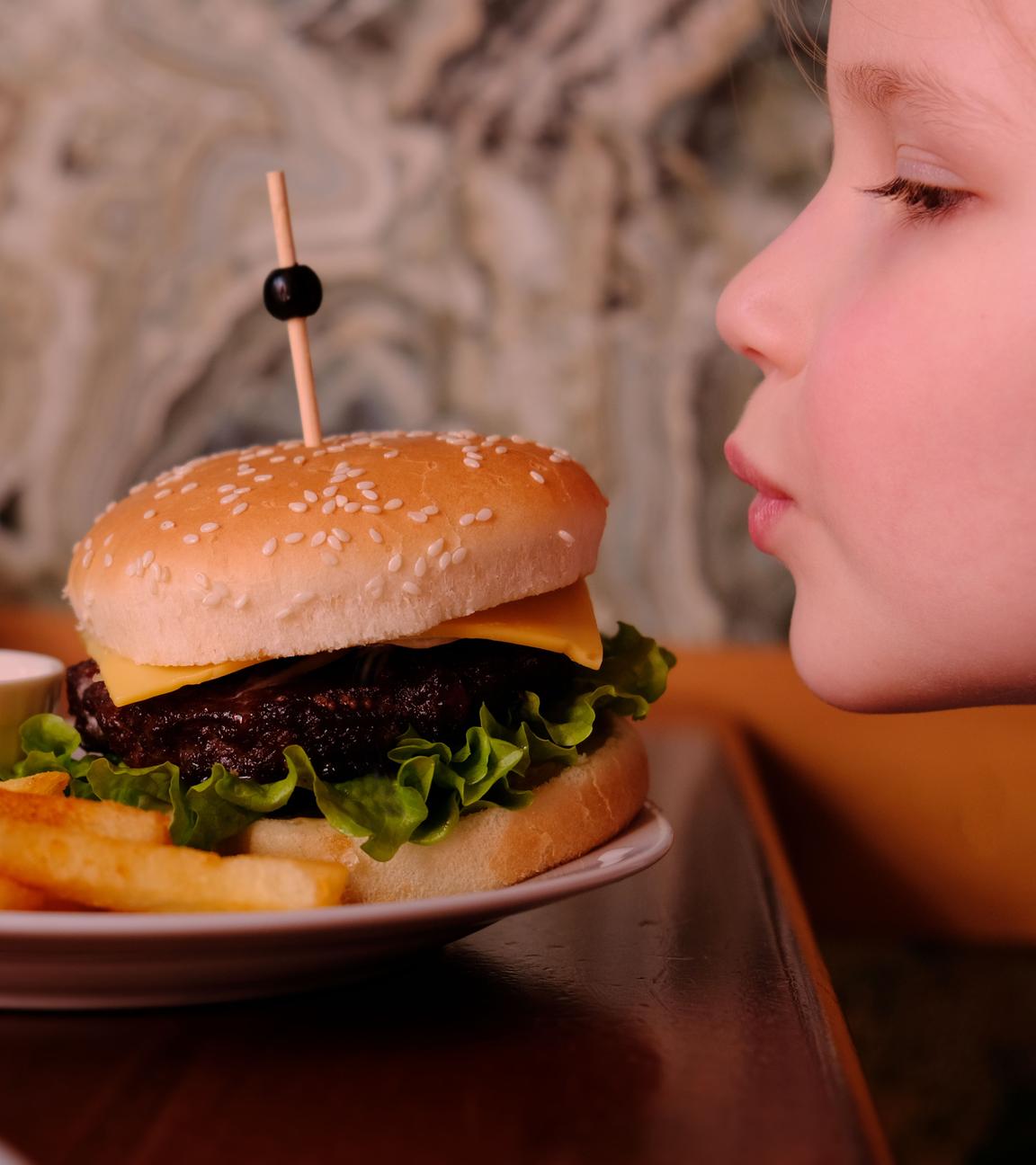 Ein Kind sitzt vor einem Burger und Pommes