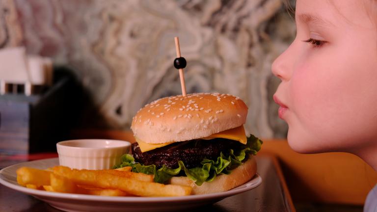 Ein Kind sitzt vor einem Burger und Pommes